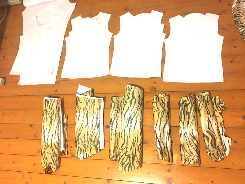 White paper sewing patterns and rolls of tiger print fabric laid out on a wooden floor.