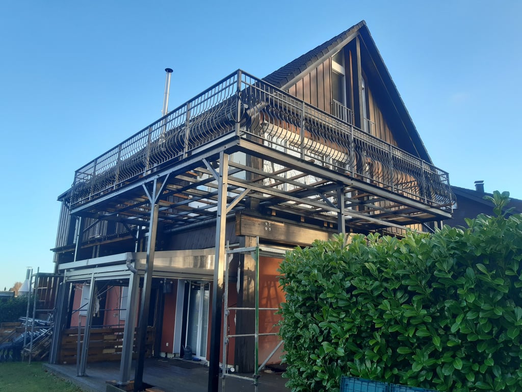 Modern house with a large elevated steel balcony structure and metal railing under a clear blue sky.