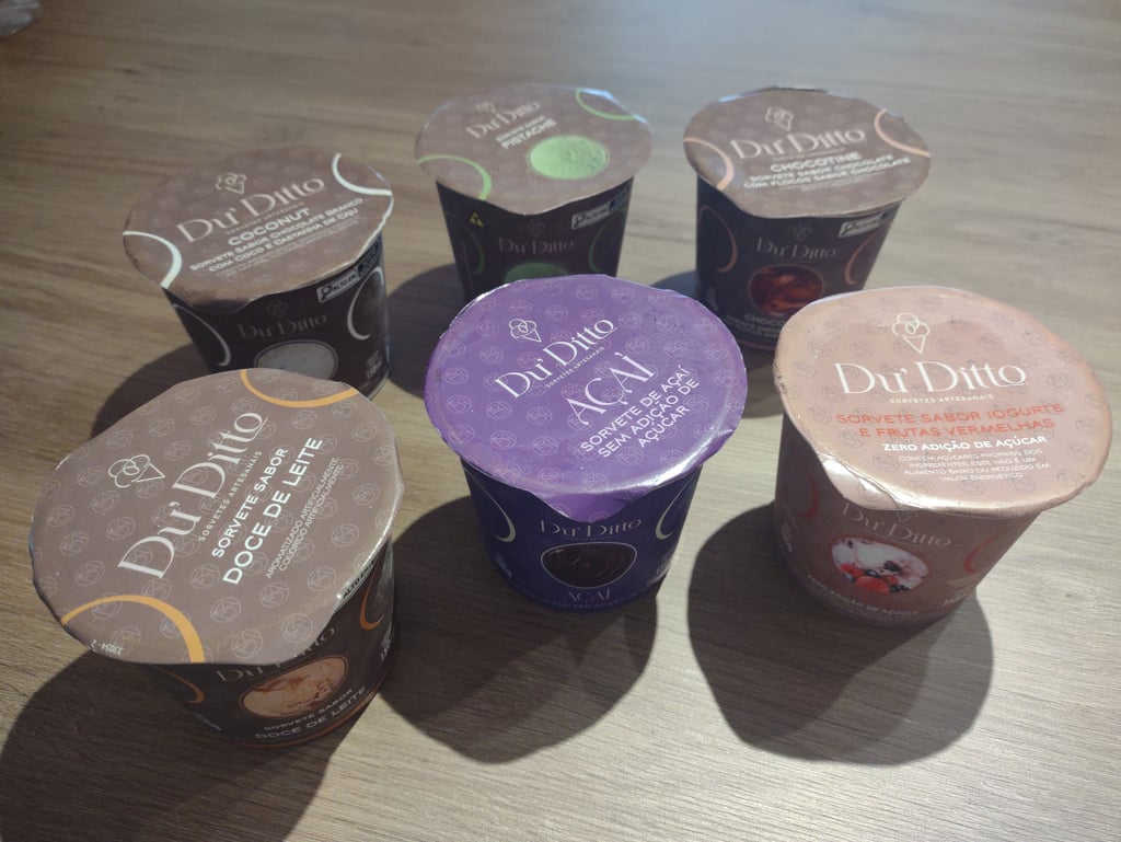 Selection of Du Ditto gourmet ice cream cups in various flavors like Acai and Dulce de Leche on a wooden surface.
