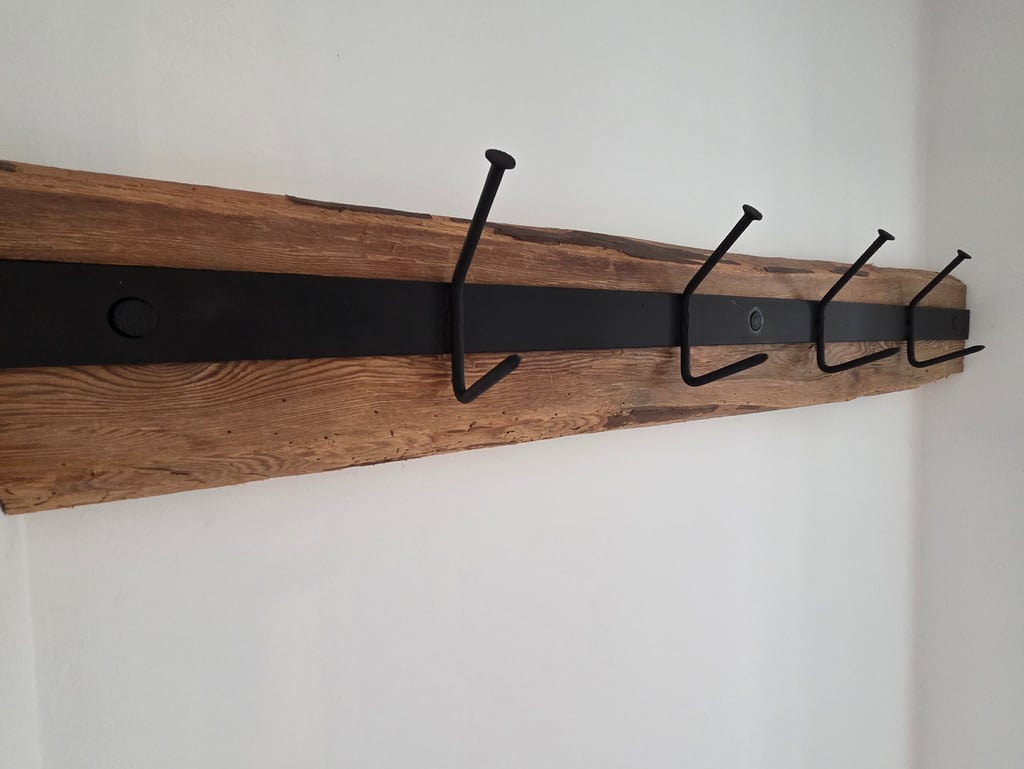 Wandgarderobe aus rustikalem Altholz mit schwarzem Metallband und vier massiven Eisenhaken im Industrial-Look.
