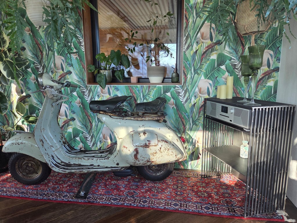 Vintage-Vespa als dekoratives Highlight vor Dschungel-Tapete neben modernem Holz-Sideboard.
