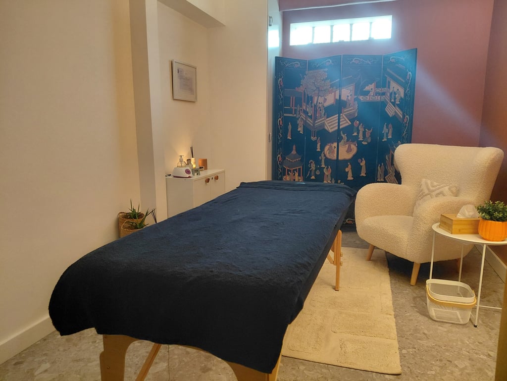 Holistic massage room with a blue therapy table, white armchair, and decorative privacy screen.