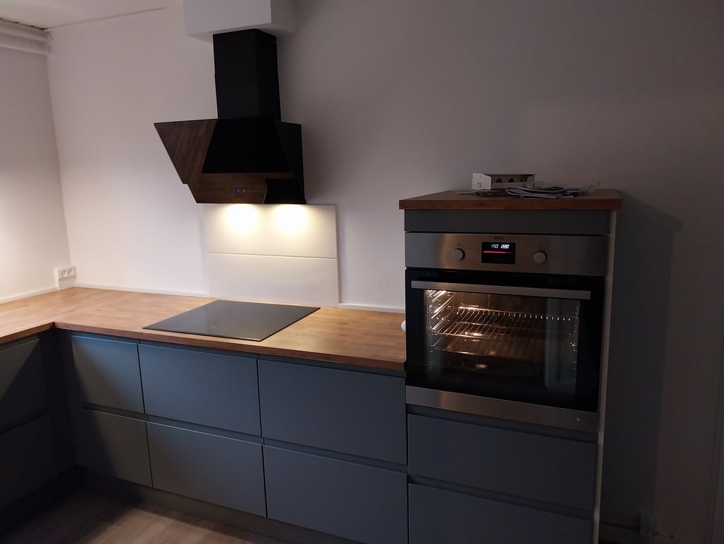 Moderne køkken med grå skabe, træbordplade, induktionskogeplade og indbygget ovn.