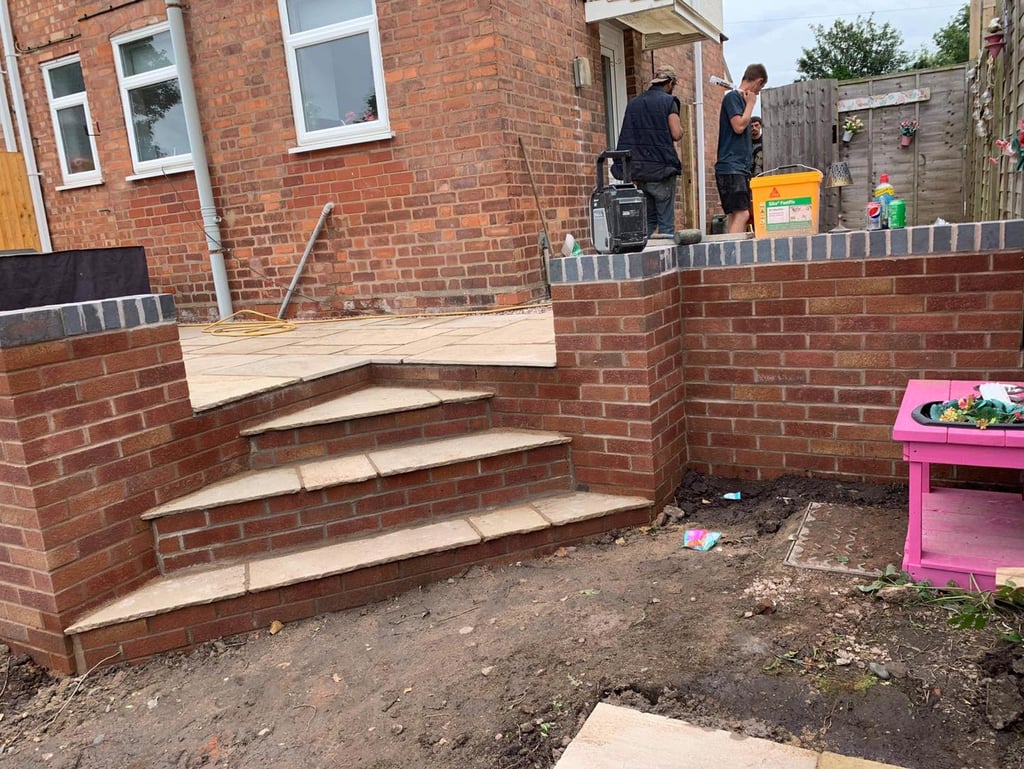 a brick wall with stairs leading up to a patio built by B R Building and Landscapes