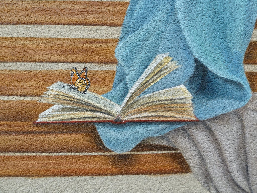 Fresque en trompe-l'oeil avec le détail d'un papillon posé sur un livre ouvert sur un banc.