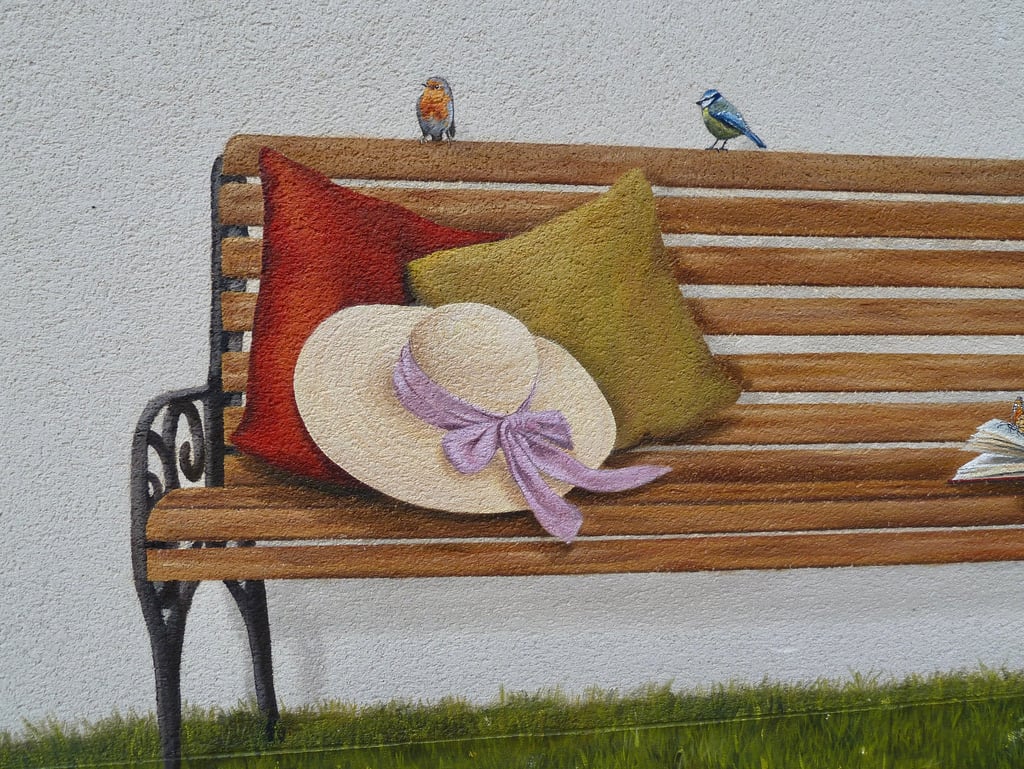 Détails d'une fresque peinte sur une façade. Tout est trompe-l'oeil: banc, oiseaux, herbe, livre,...