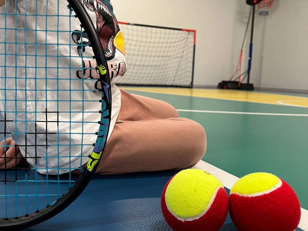 Primo piano di una racchetta da tennis e due palline rosse e gialle su un campo multisport nella palestra Move 2 Grow a Milan