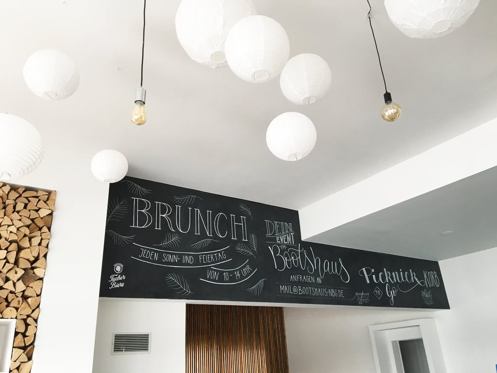 Handwritten brunch menu on a black chalkboard wall decorated with white paper lanterns and light bulbs.