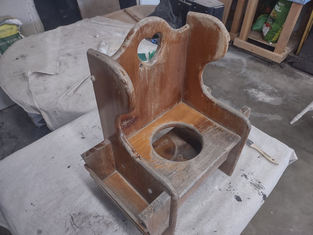 Vintage wooden potty chair with a worn finish undergoing restoration in a workshop setting.