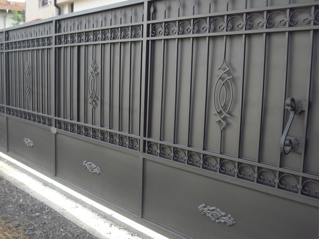 Elegant black ornamental wrought iron driveway gate with decorative scrollwork and a solid privacy base.