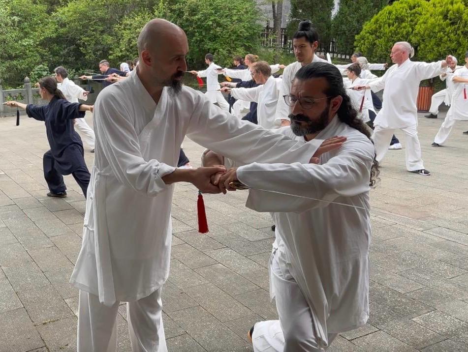 Ismet Himmet guiding Mehmet Başkak during a Tai Ji form correction at an outdoor group training.