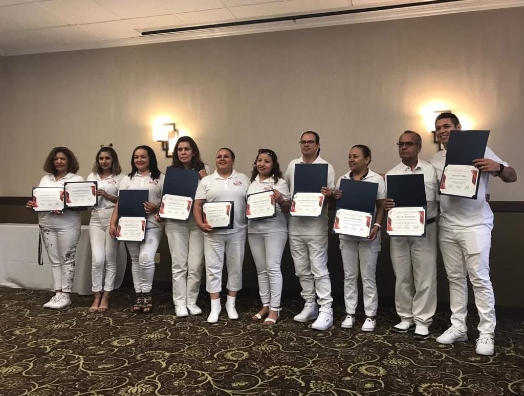 A group of diverse professionals in white uniforms holding graduation certificates at a ceremony.