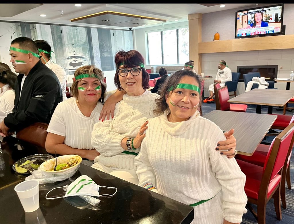 Three women in white sweaters and green headbands celebrating at a restaurant.