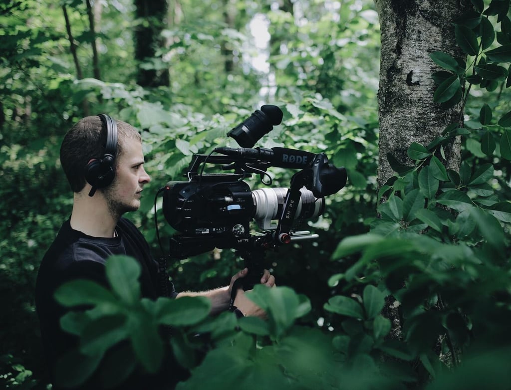 A professional videographer using a cinema camera with a Rode microphone to film in a lush green forest.
