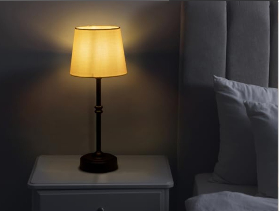 Elegant bronze bedside table lamp with a warm glowing fabric shade on a white nightstand.