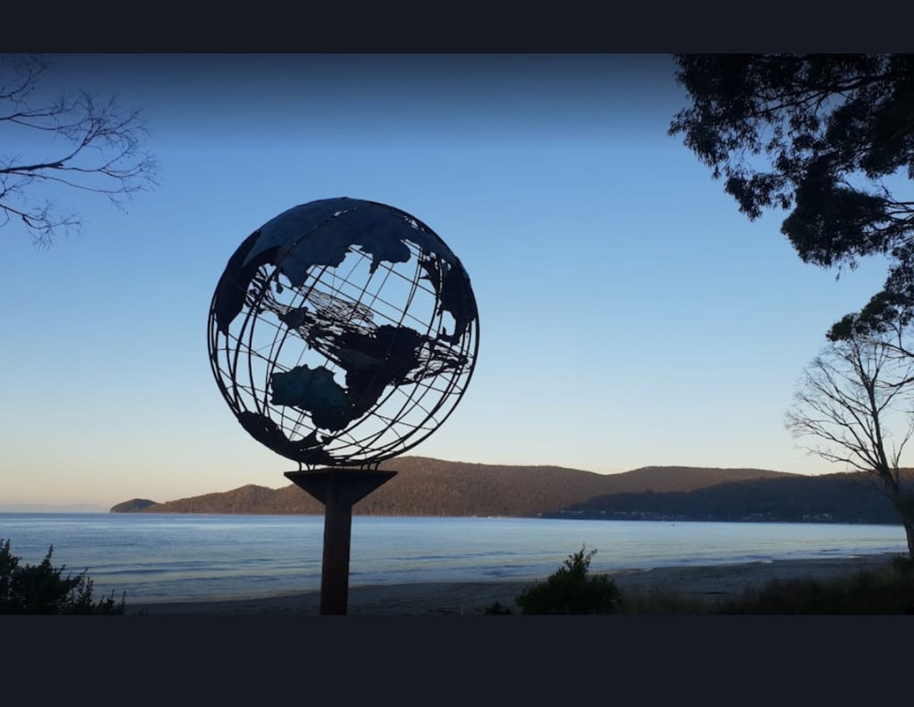 Verdigris metal globe sculpture on the beach with a mother whale and her calf in the middle of it