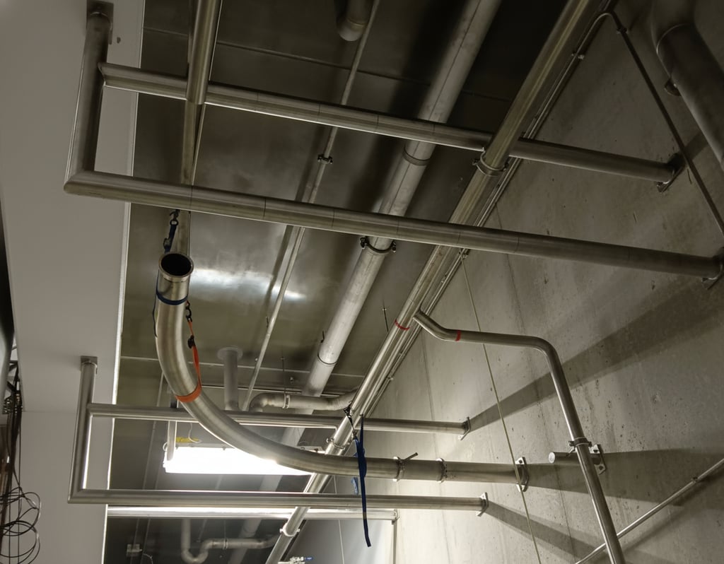Stainless steel piping network and plumbing installed along a concrete wall.