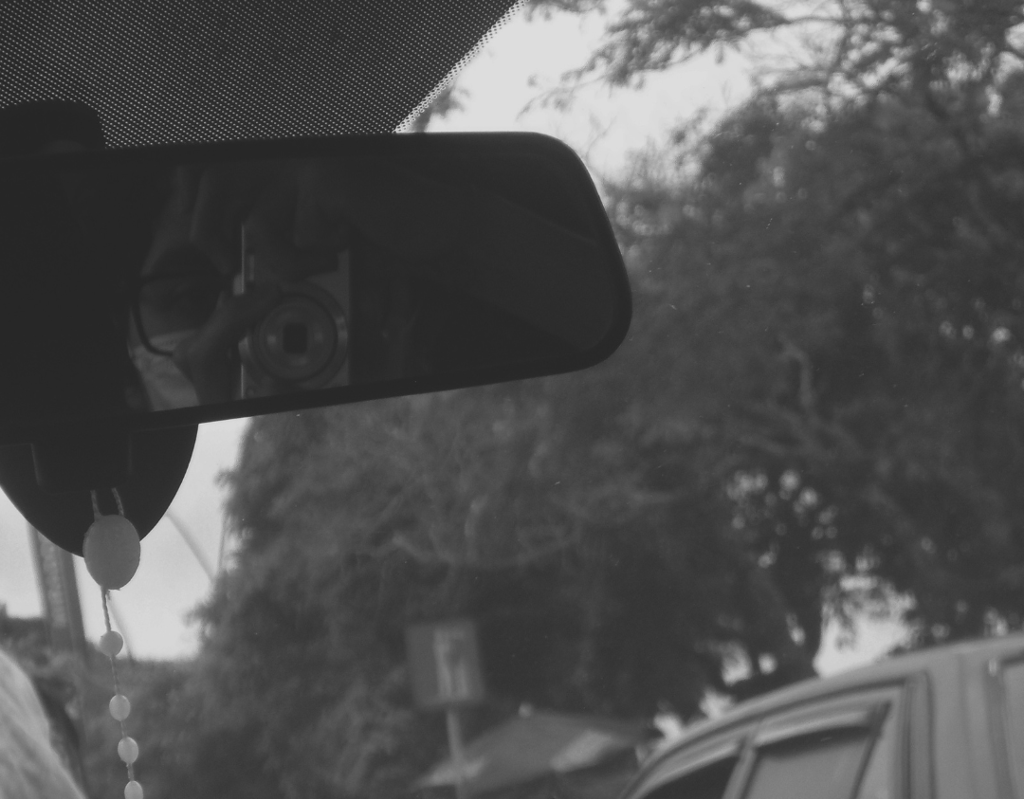 Reflejo de fotógrafo en el retrovisor de un auto entre árboles.
