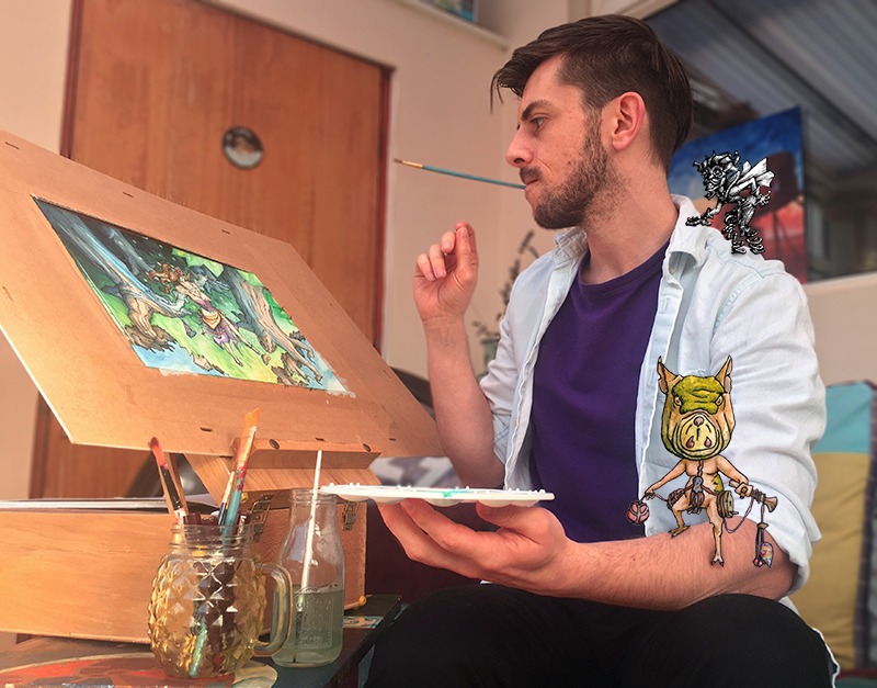 A handsome young male artist with dark hair and blue shirt sits at his easel of fantasy art