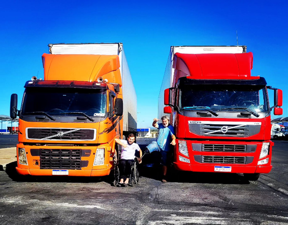 dois grandes caminhões com dois caminhoneiros junto aos caminhões onde um é cadeirante