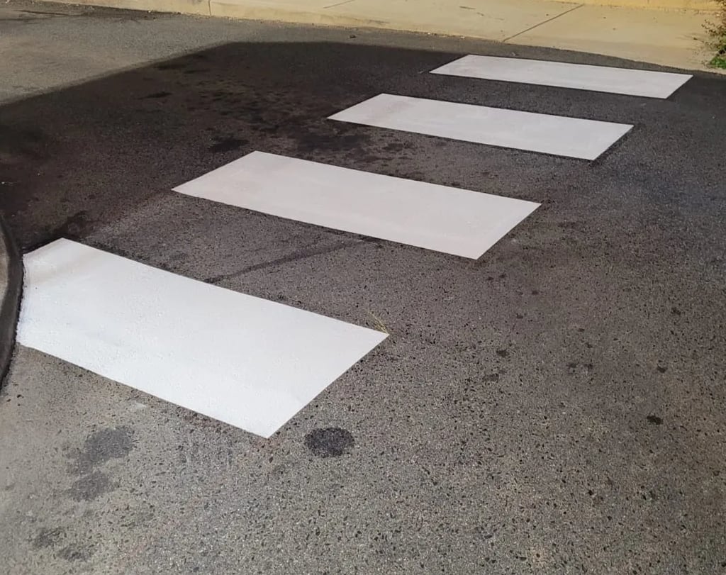 High-visibility white crosswalk stripes on curved blacktop pavement.