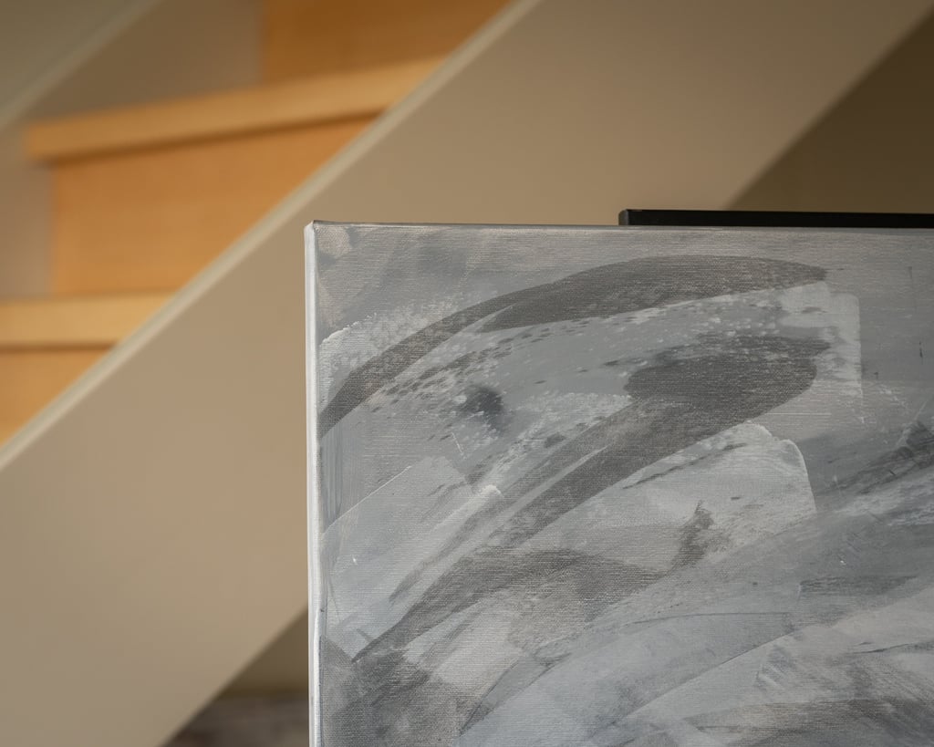 Close-up of a grey abstract canvas painting on an easel in a modern home with wooden stairs.