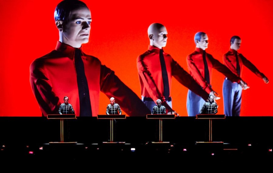 Iconic image of Kraftwerk standing at synthesizers with a rigid, robot-like performance style.