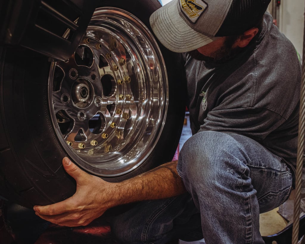 A mechanic installing a custom chrome wheel and performance tire on a vehicle.