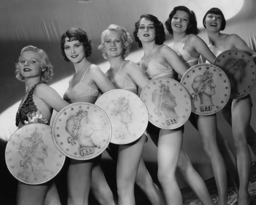 Low‑angle shot of Gold Diggers of 1933 chorus girls holding giant coins in “We’re in the Money.”