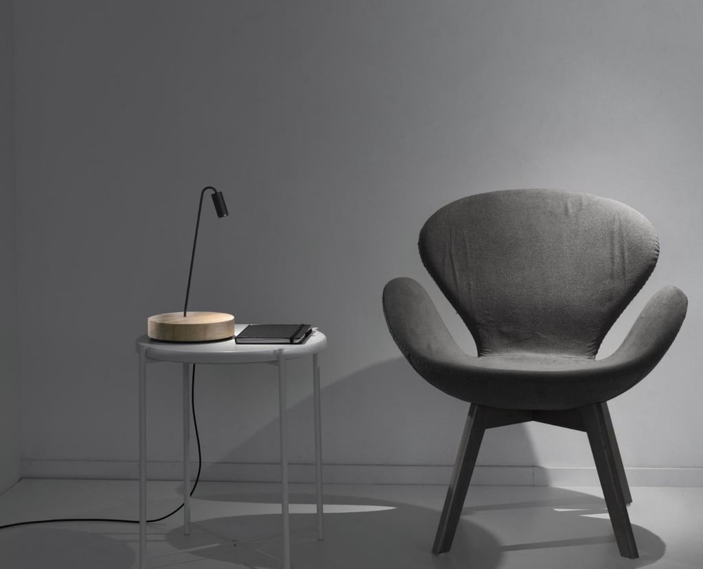 Lámpara de sobremesa con base circular junto a butaca en ambiente de lectura moderno
