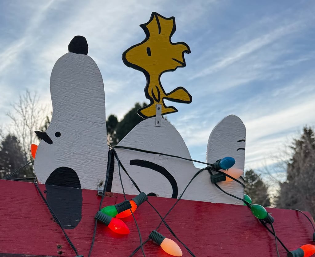 Lawn decoration of Snoopy and Woodstock on a red dog house wrapped in Christmas lights