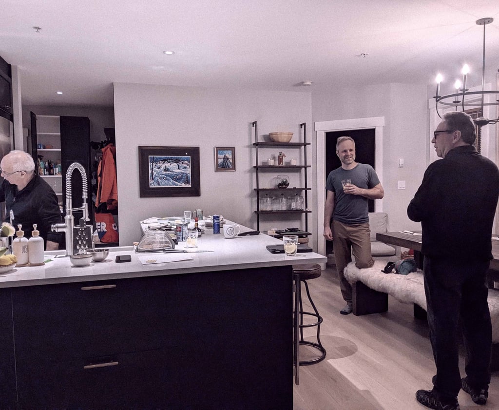 Three men talking and preparing food together around a kitchen island in a home kitchen.