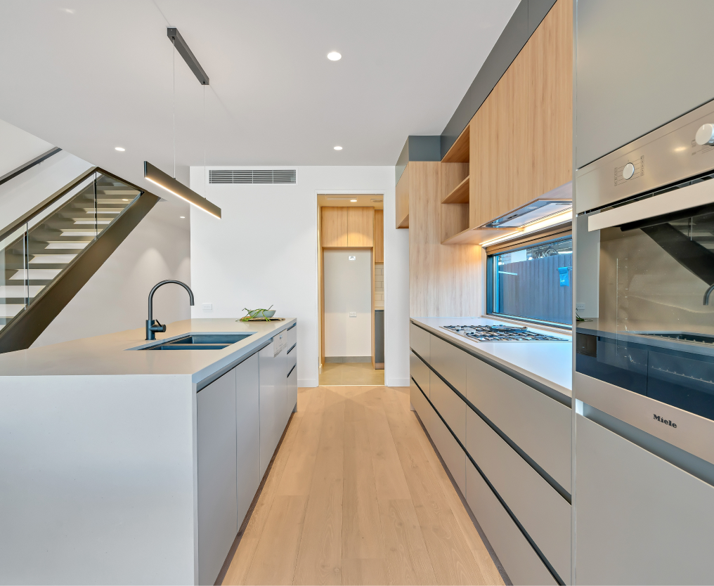 Modern kitchen with sleek cabinetry, built-in appliances, and under-stair sink area