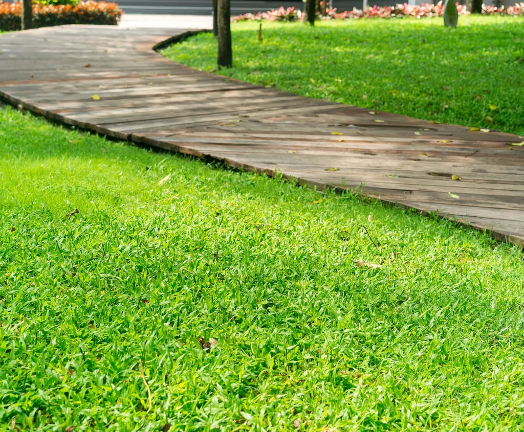 Curved wooden garden walkway winding through a lush green lawn in a landscaped park.
