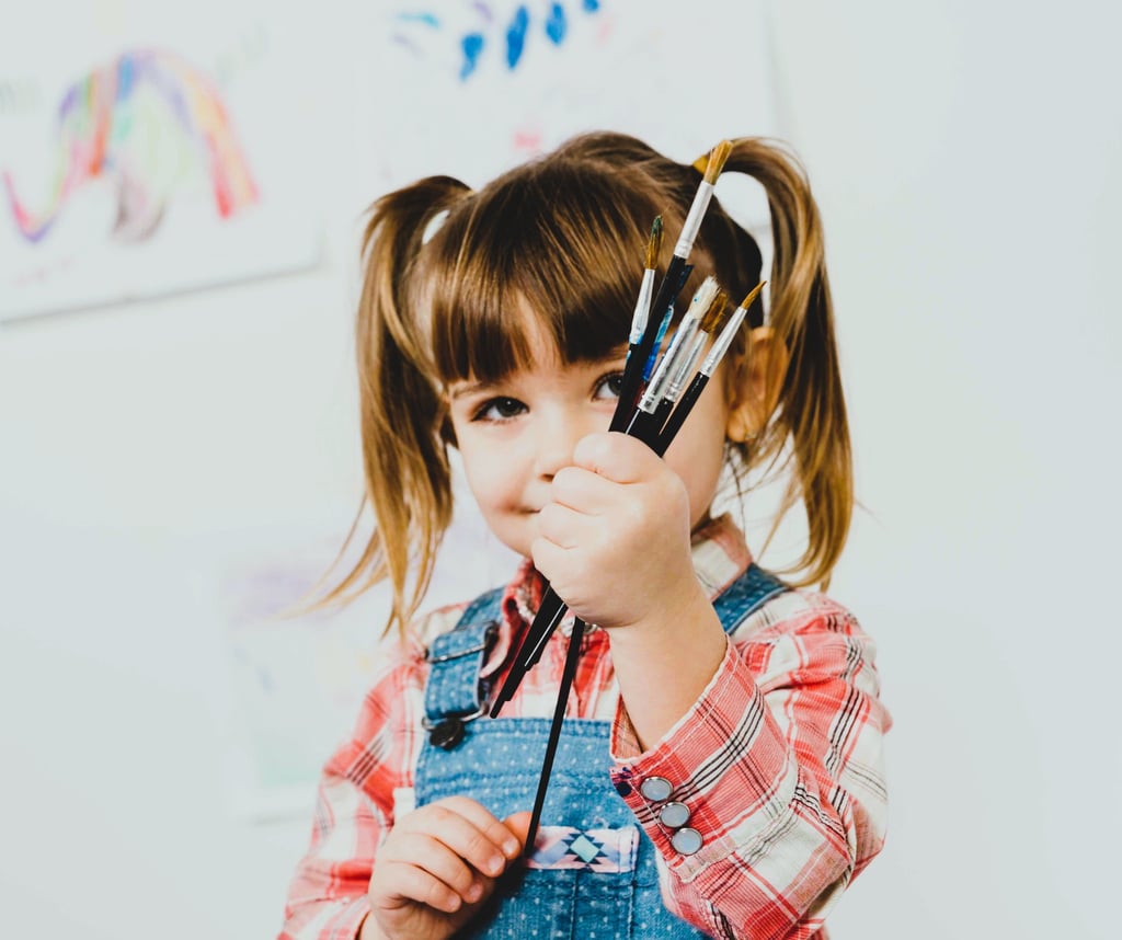 A happy girl standing with paint brushes hands.