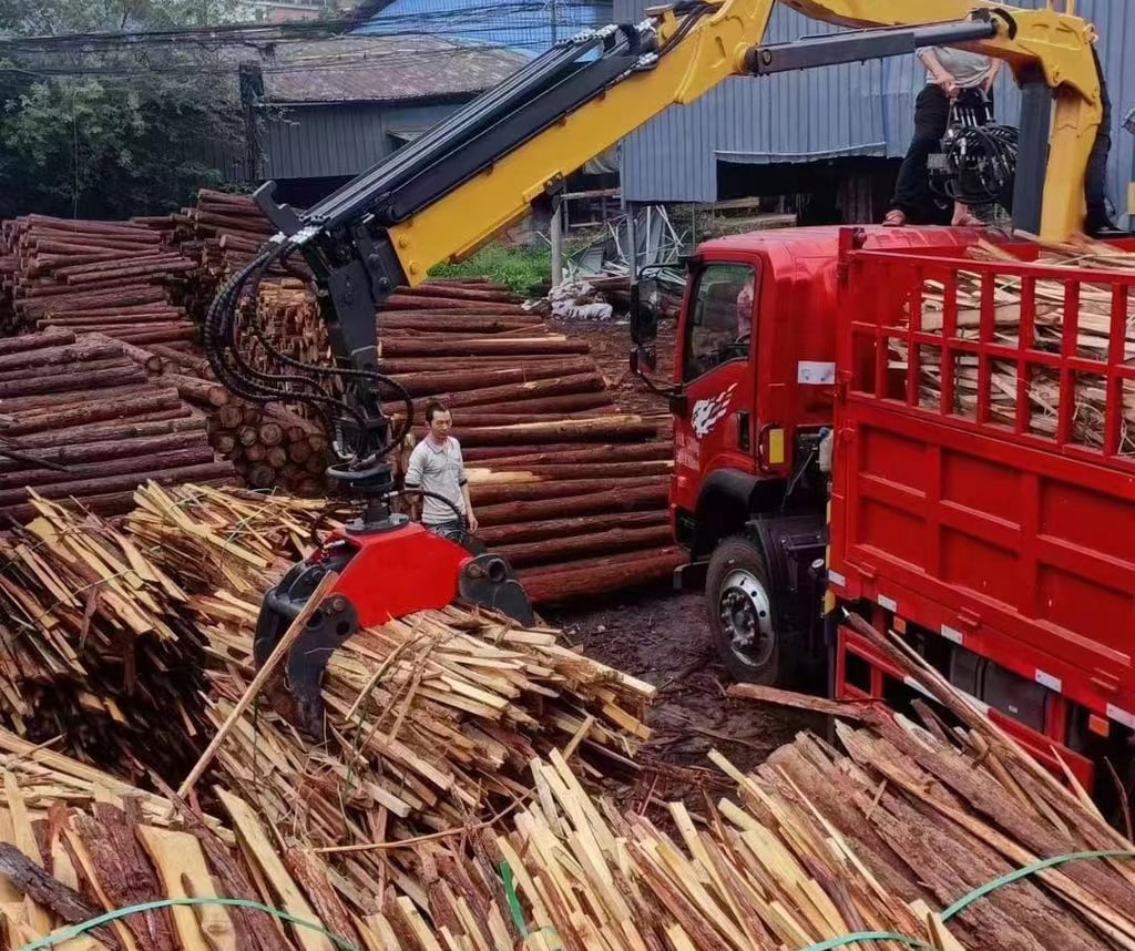 A knuckle boom truck crane loading a large pile of wood onto a truck.