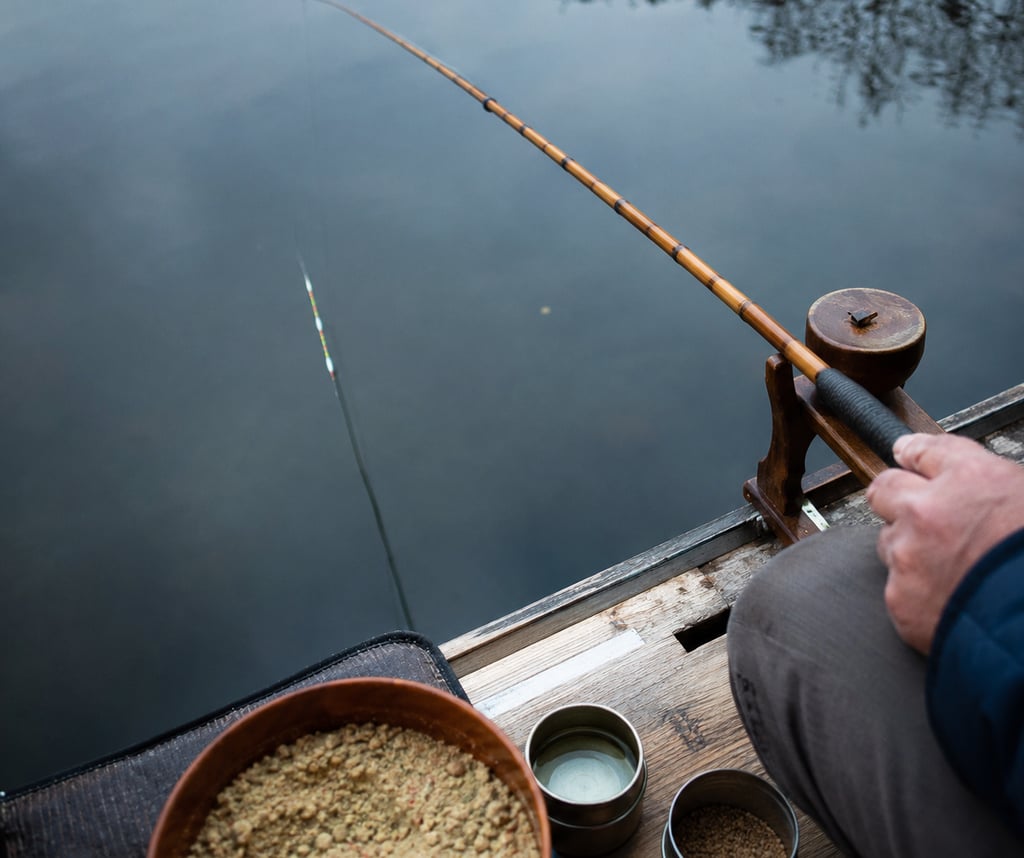 A person using a vintage bamboo fishing rod with bait bowls while fishing on a calm lake.