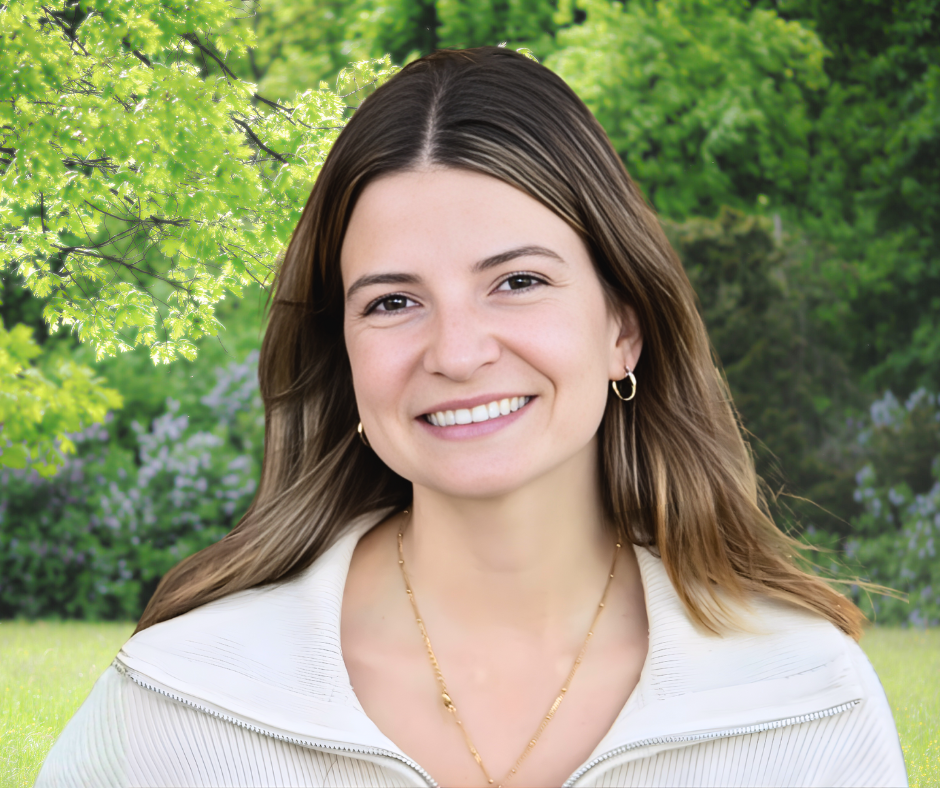 Smiling woman with light brown hair wearing a white sweater in a sunny green park setting.