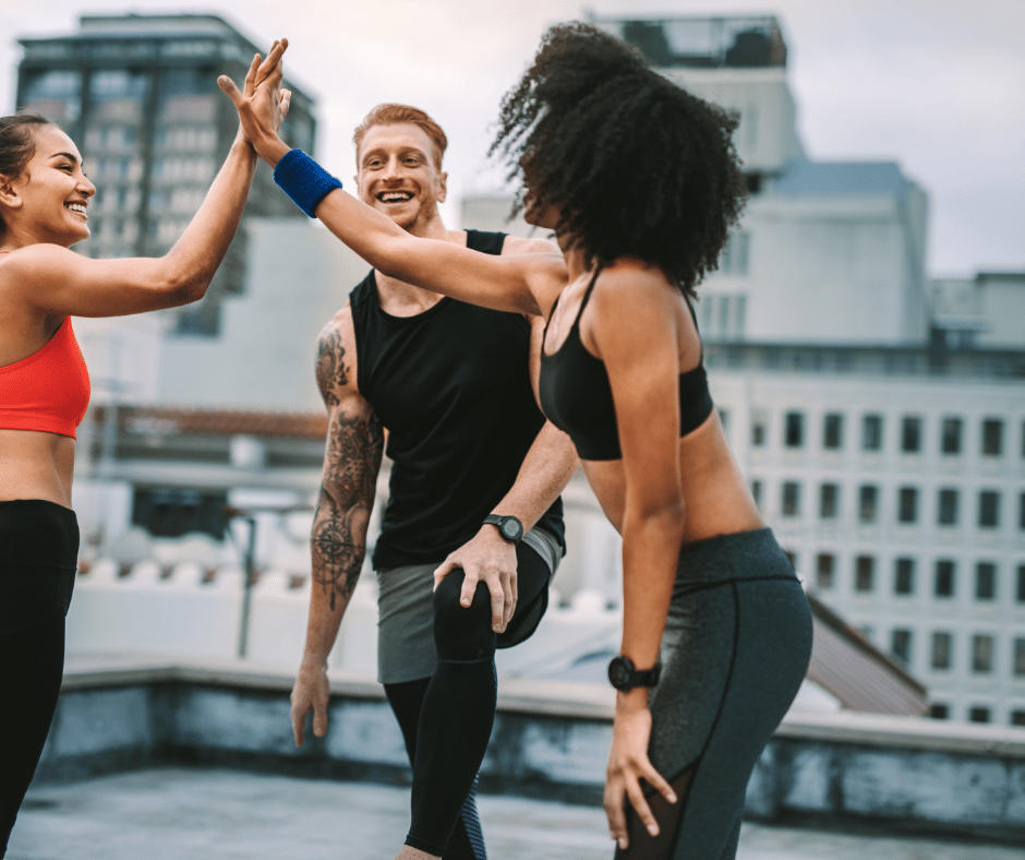 Smiling diverse friends giving high-fives during a rooftop outdoor workout session in the city.