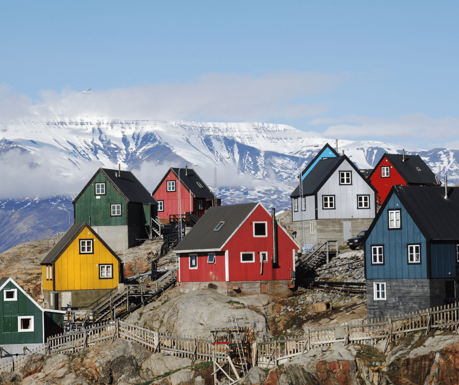Colorful coastal houses in a Greenland village with snow-capped mountains in the background.