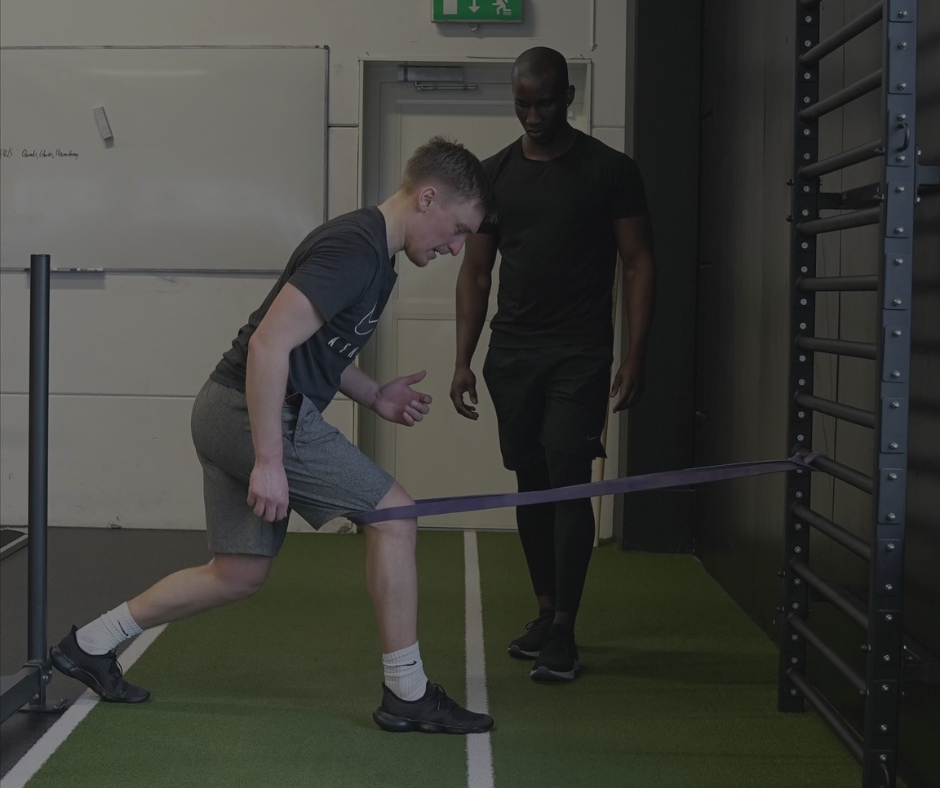 A personal trainer assists a man performing resistance band lunges for physical therapy in a gym.