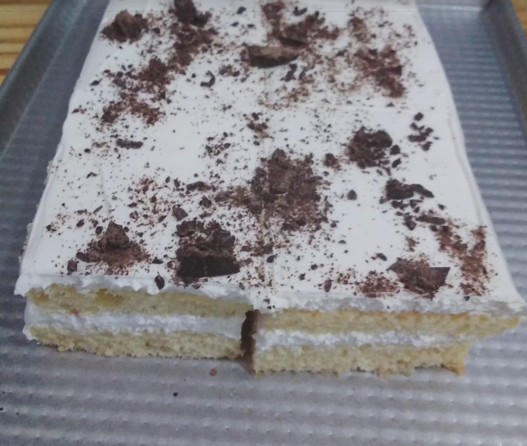 Layered vanilla sponge cake with white frosting and dark chocolate shavings on a baking sheet.