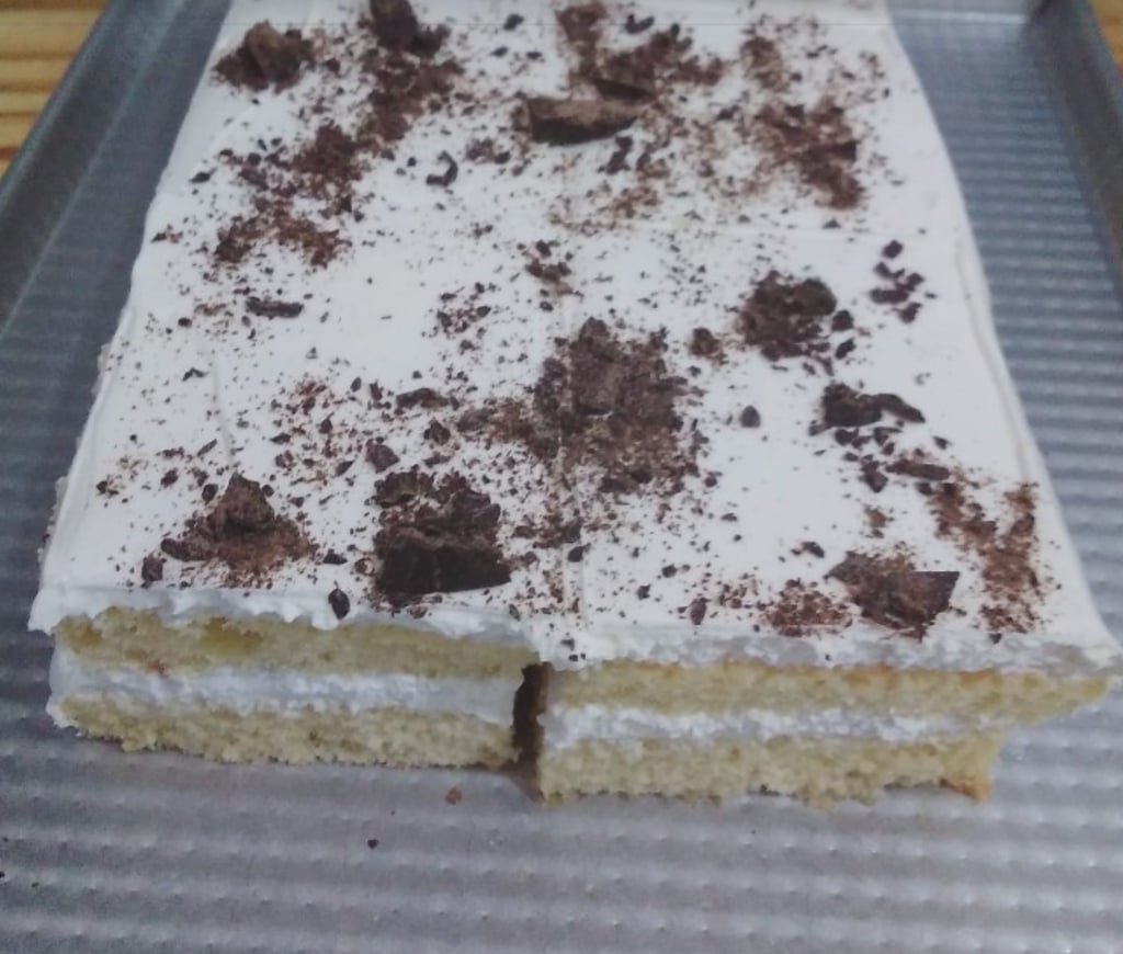 Layered vanilla sponge cake with white frosting and dark chocolate shavings on a baking sheet.