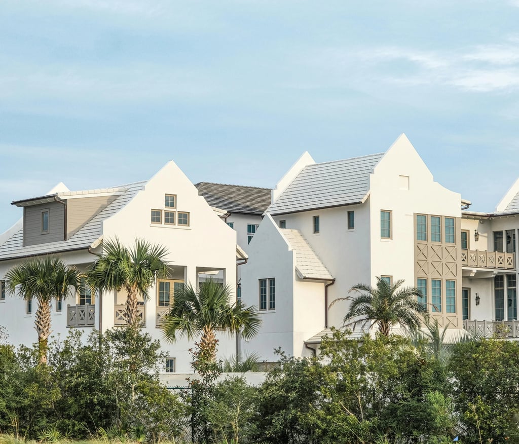 Luxury white coastal villas with palm trees and modern architecture under a blue sky.