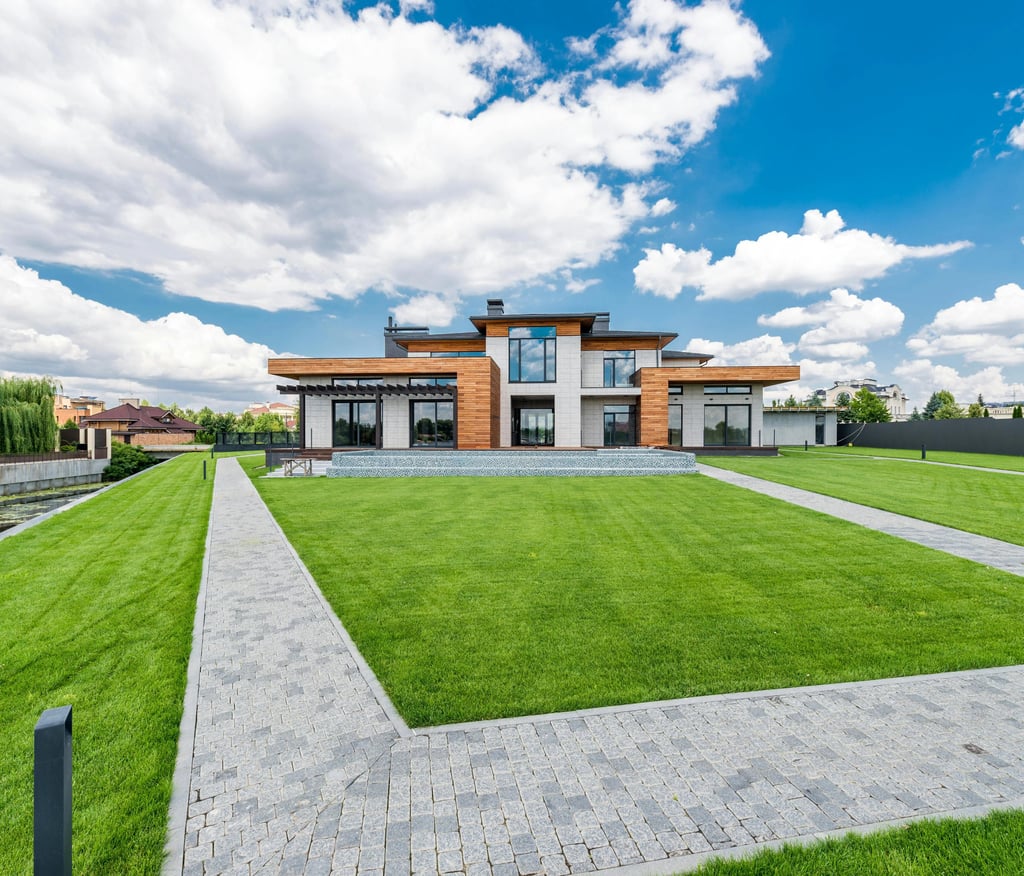 Modern luxury house with a manicured green lawn and stone walkway under a blue sky.