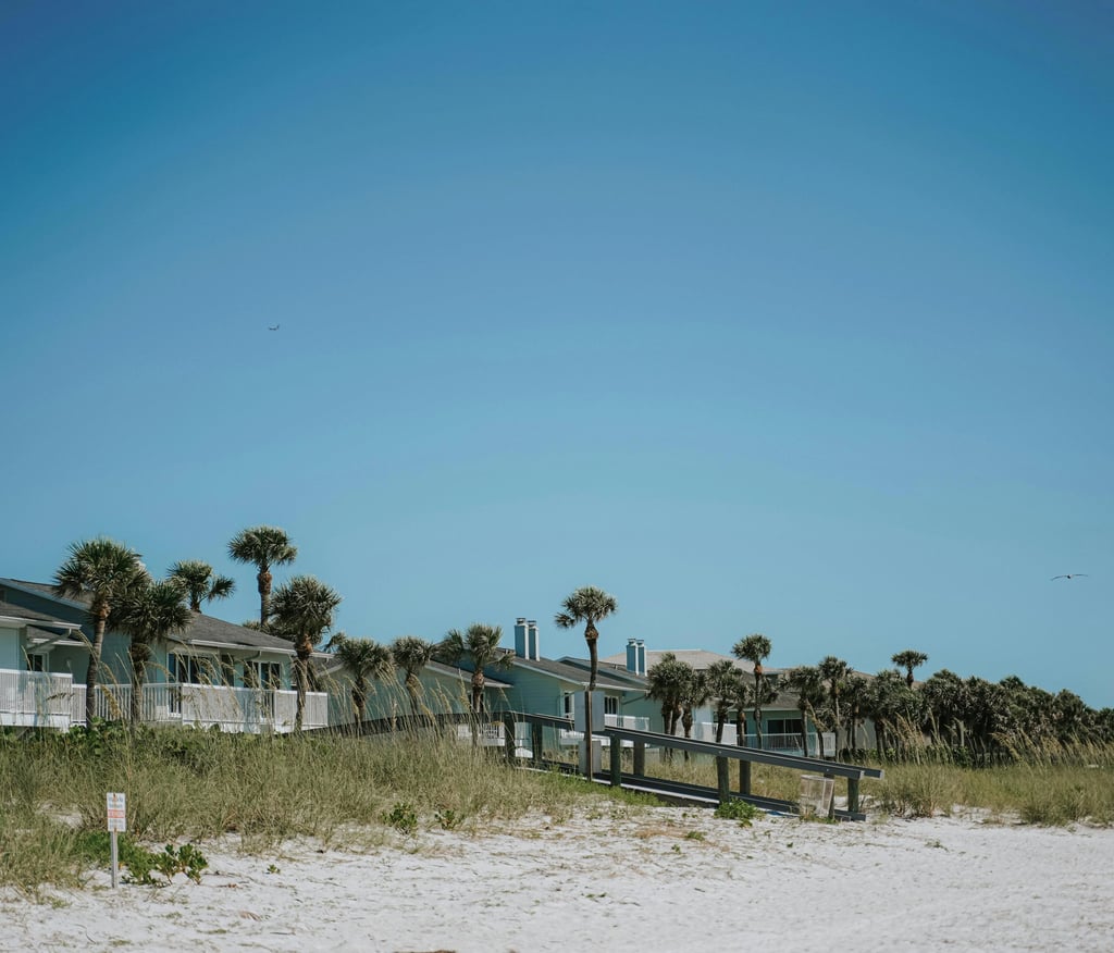 Luxury beachfront vacation rentals with palm trees and a wooden boardwalk on a sunny beach.