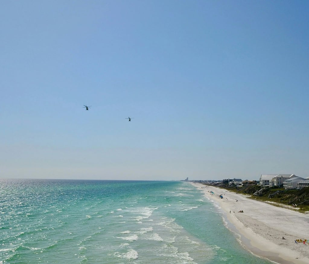 Two helicopters flying over turquoise ocean water and white sand beaches of a coastal resort town.