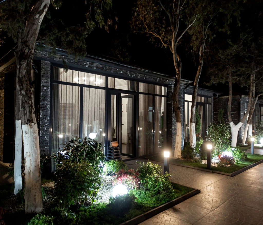 Modern glass cabin architecture with warm night lighting and landscaped garden pathway.