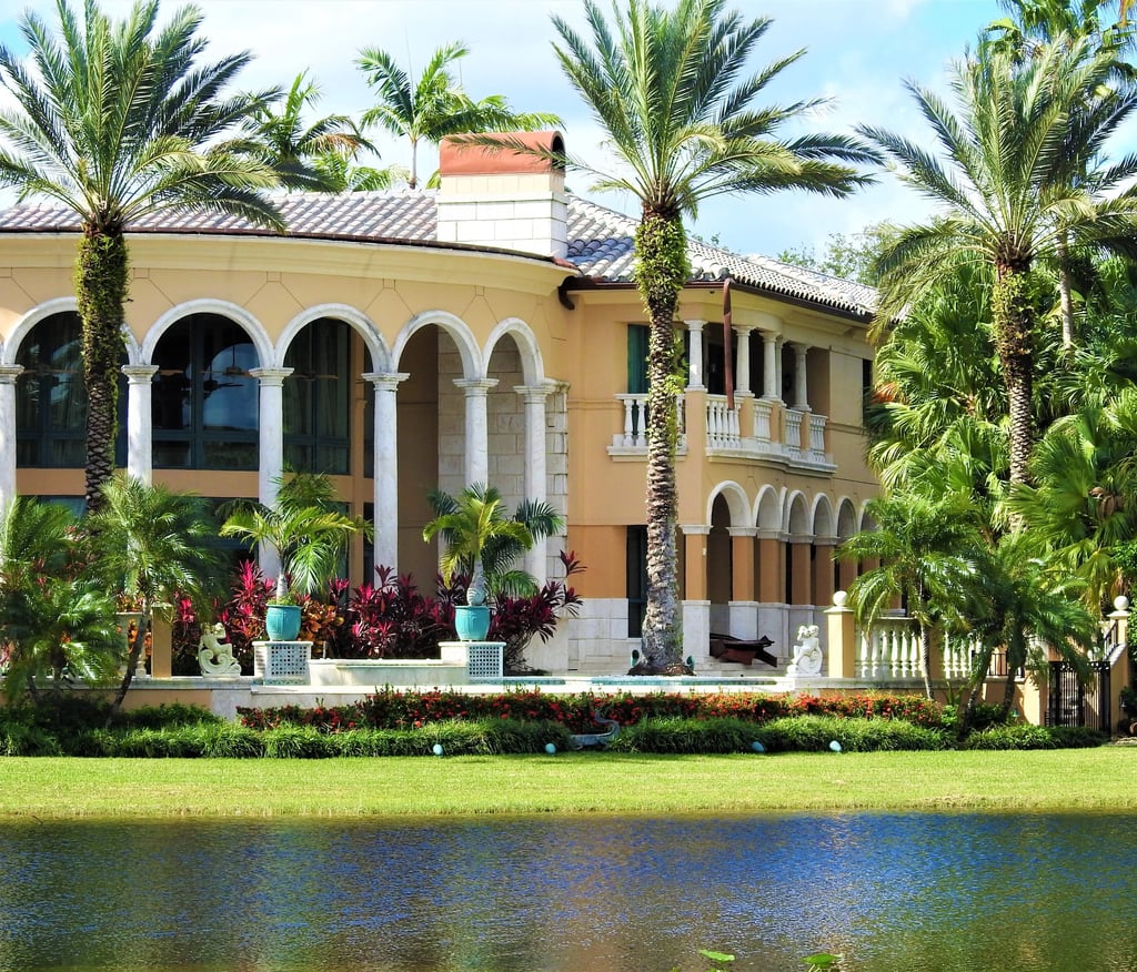 Luxury Mediterranean style waterfront mansion with arched windows and tropical palm trees.