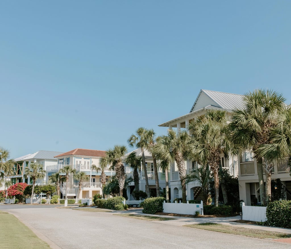 Luxury beach vacation rentals and palm trees along a quiet coastal street under a clear blue sky.